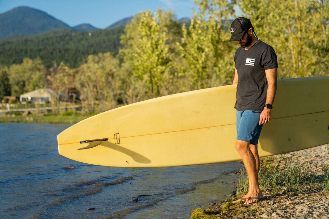 Man wearing UPF clothing holding paddleboard by lake